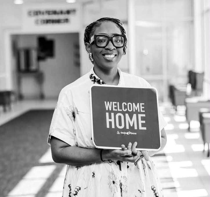 A smiling woman holding a Welcome Home sign